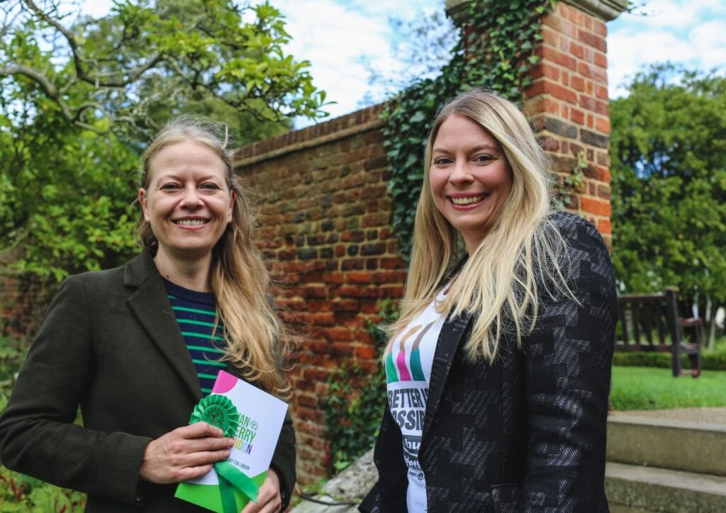Portrait of Sian Berry and Lorna Jane Russell carrying Green Party paraphernalia